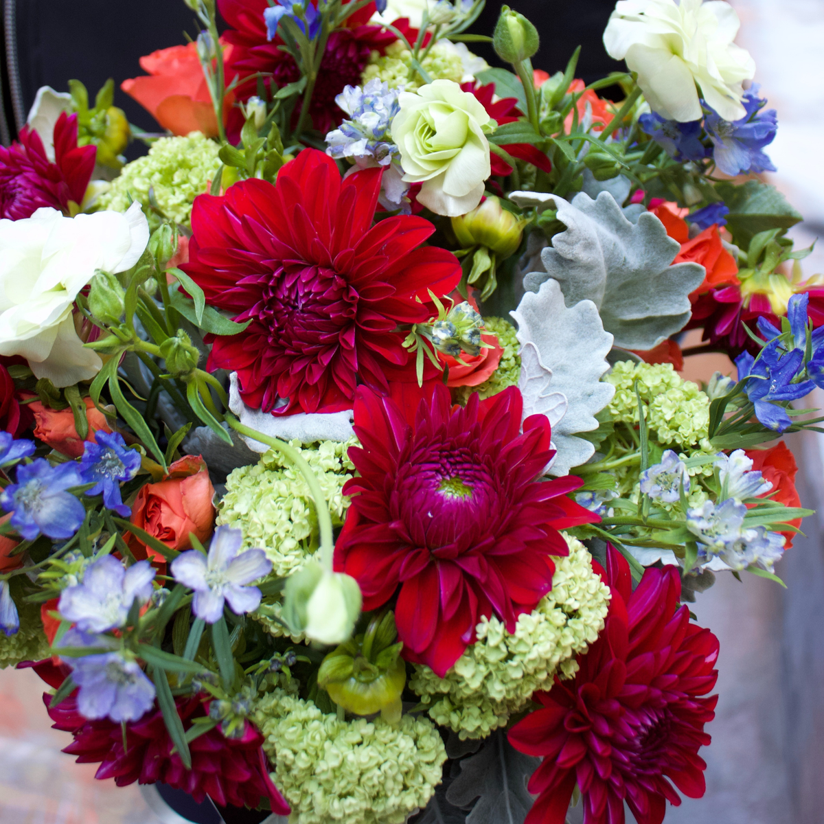 Bouquet of red, white, orange, blue, and green flowers with assorted greenery.