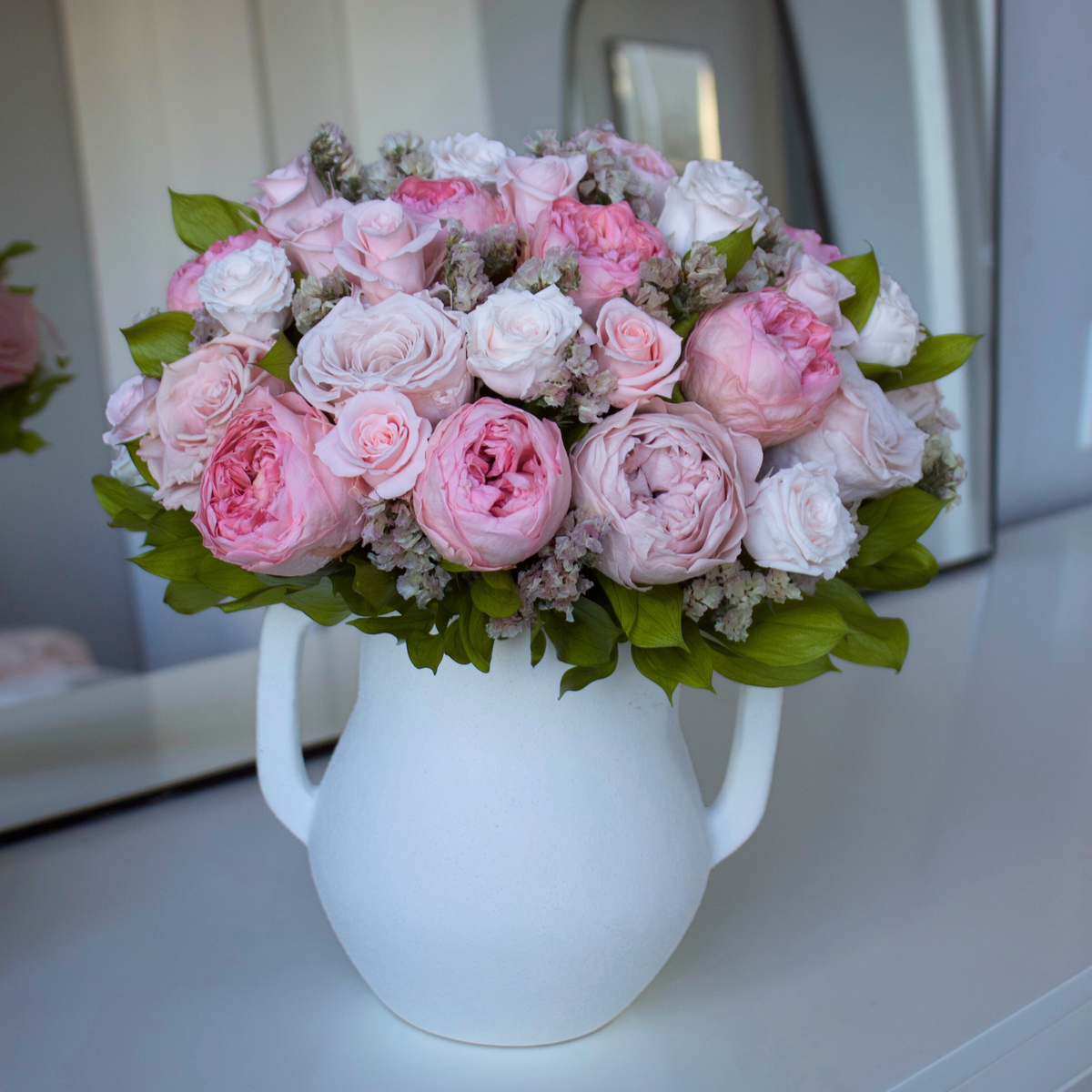 The Paloma by Eos Blooms: preserved pink and white roses in a white vase on a white table.