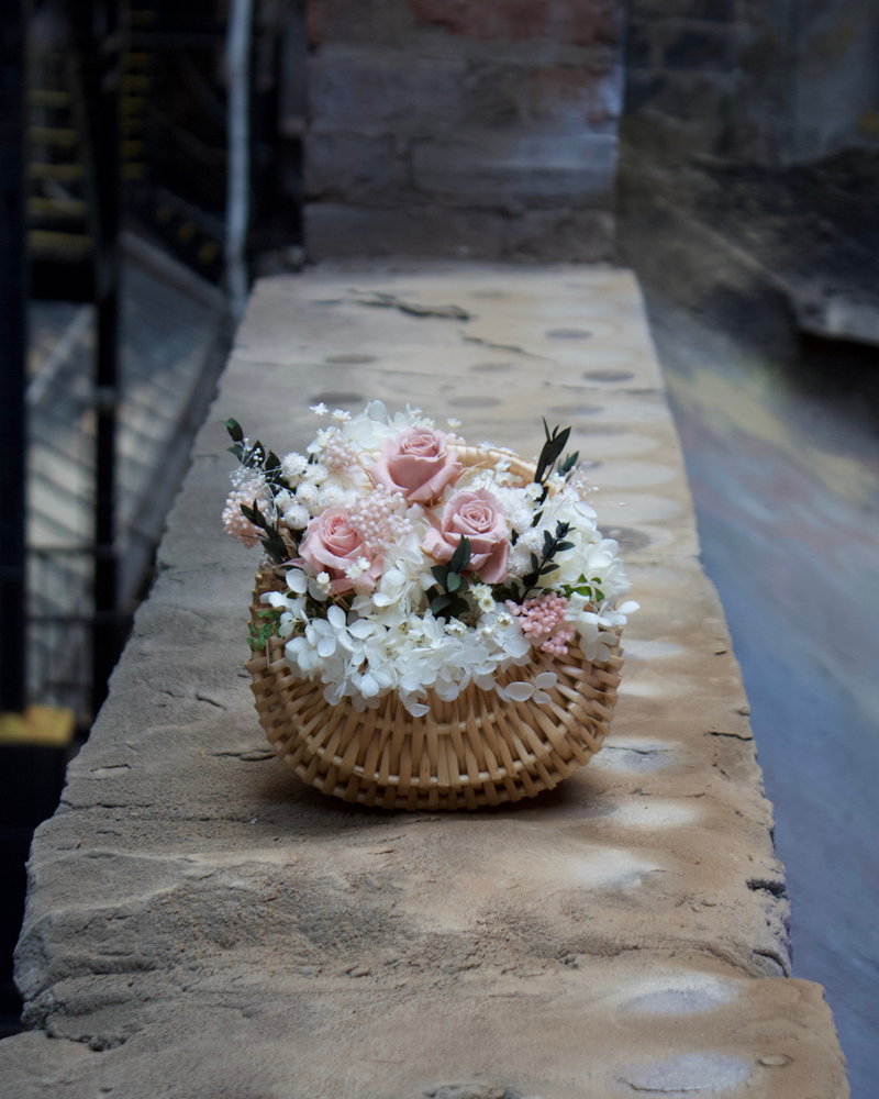 Eos Blooms Mini Cottage Basket with pink and white flowers on a stone ledge outdoors.