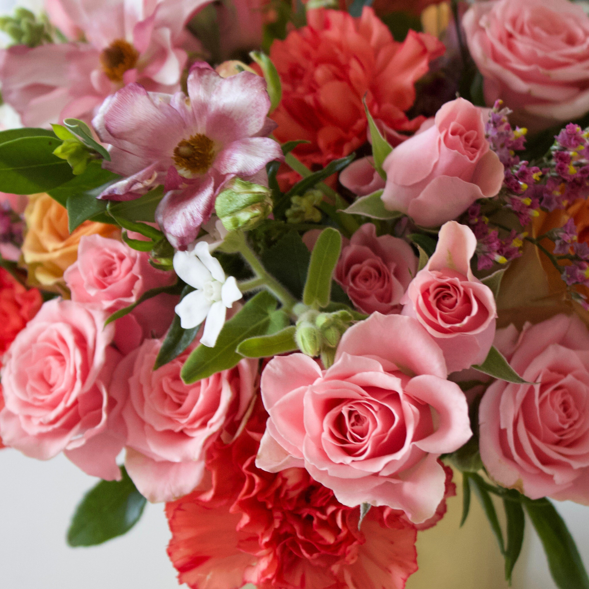 Bouquet of pink roses and assorted flowers with green leaves in soft natural light.