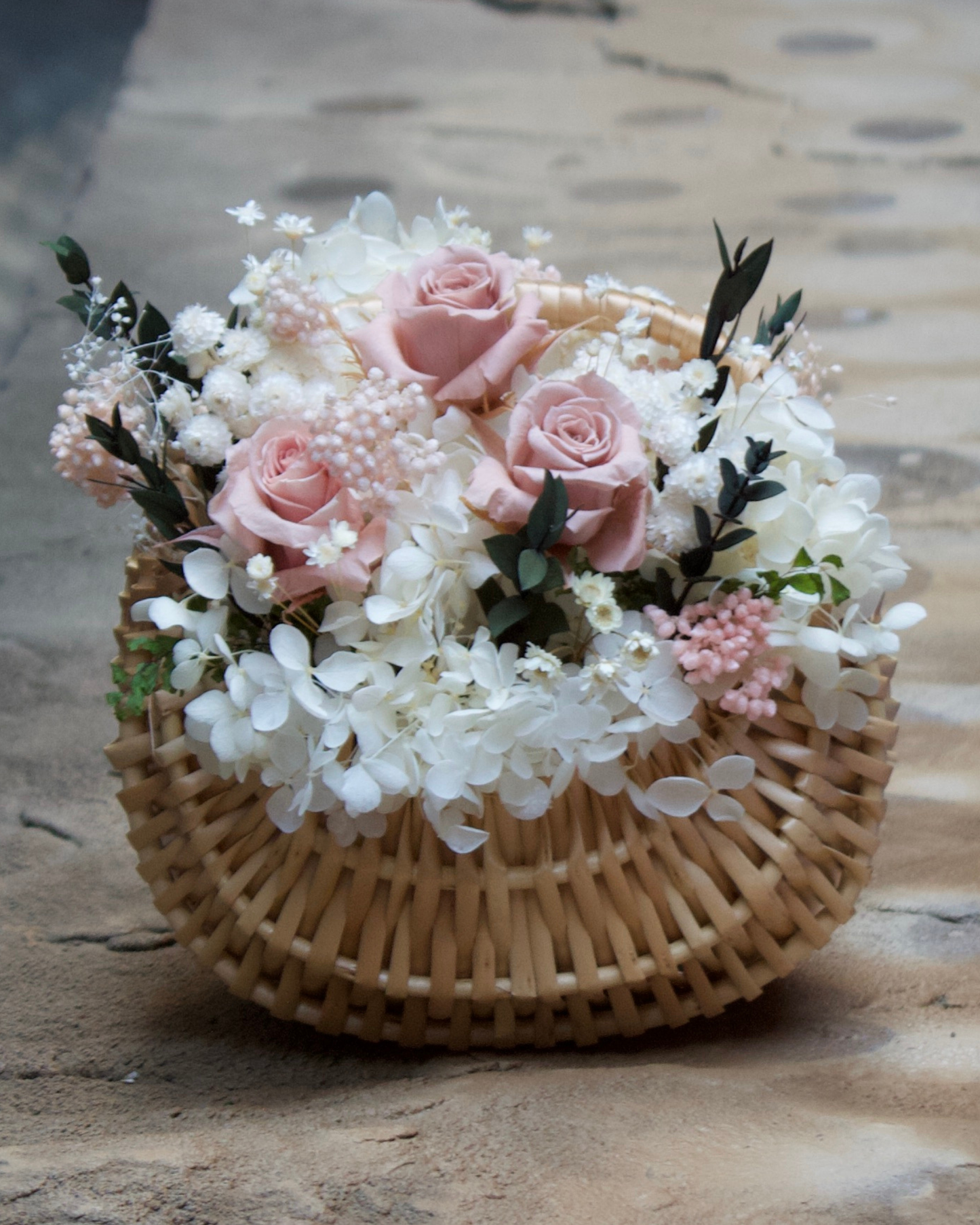Eos Blooms Mini Cottage Basket with preserved roses and white blooms on a stone surface.