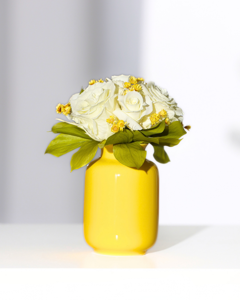 Eos Blooms Mini Milk Jar with Forever Roses and yellow preserved flowers on a white surface.