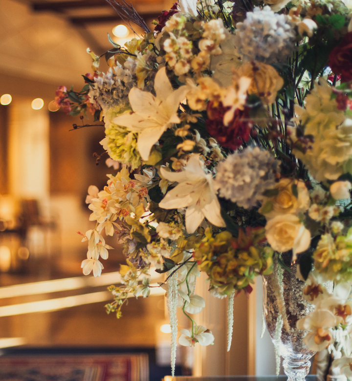 A large, elegant bouquet of assorted flowers in a glass vase, softly lit indoors.
