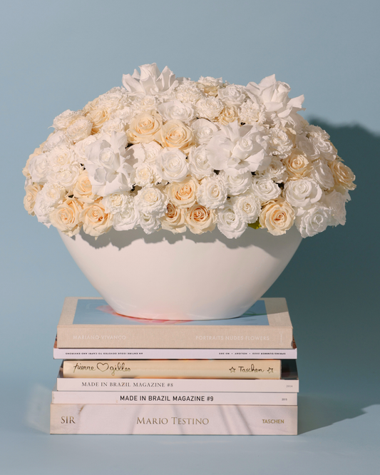 Aeterna Privé by Eos Blooms: white rose bowl on books, luxe floral look, blue background.