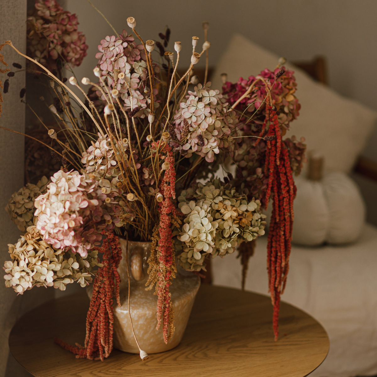 Eos Blooms Preserved Hydrangeas in a vase on a wooden table beside a beige sofa.