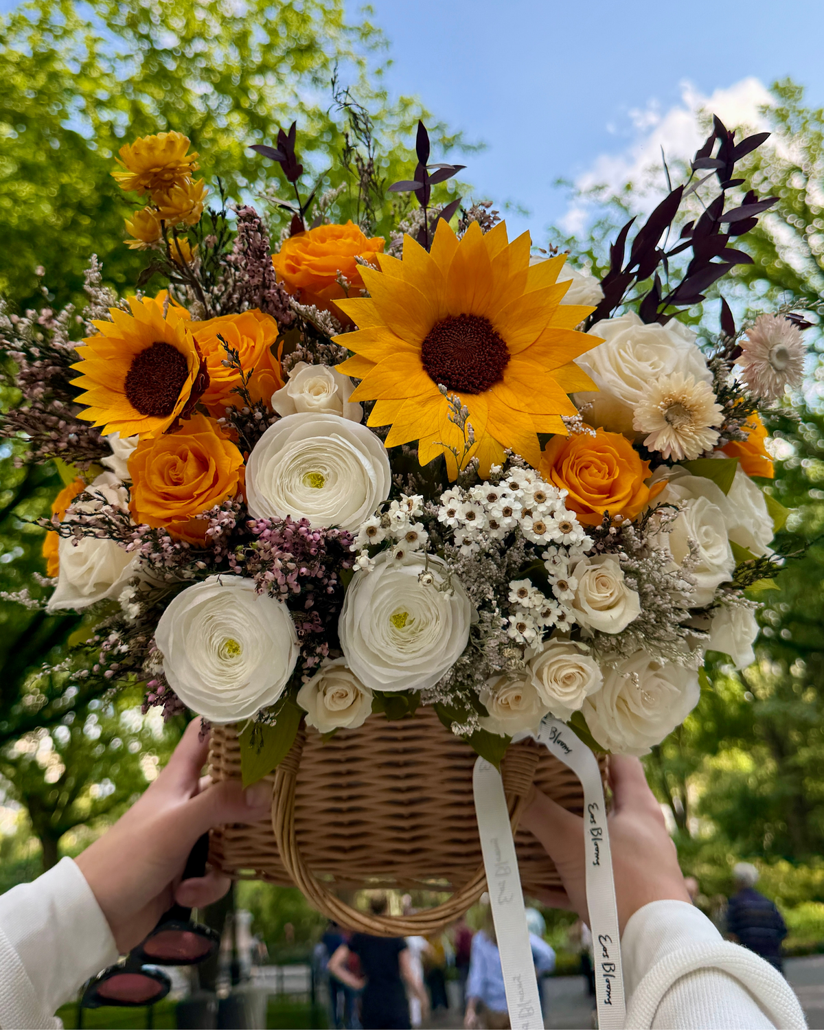Hands holding Eos Blooms’ The Orchard | Autumn Basket with sunflowers, roses, and white blooms.