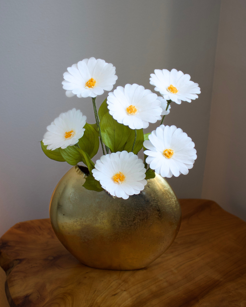 The Margarita preserved daisies by Eos Blooms in a gold vase on a wooden table.