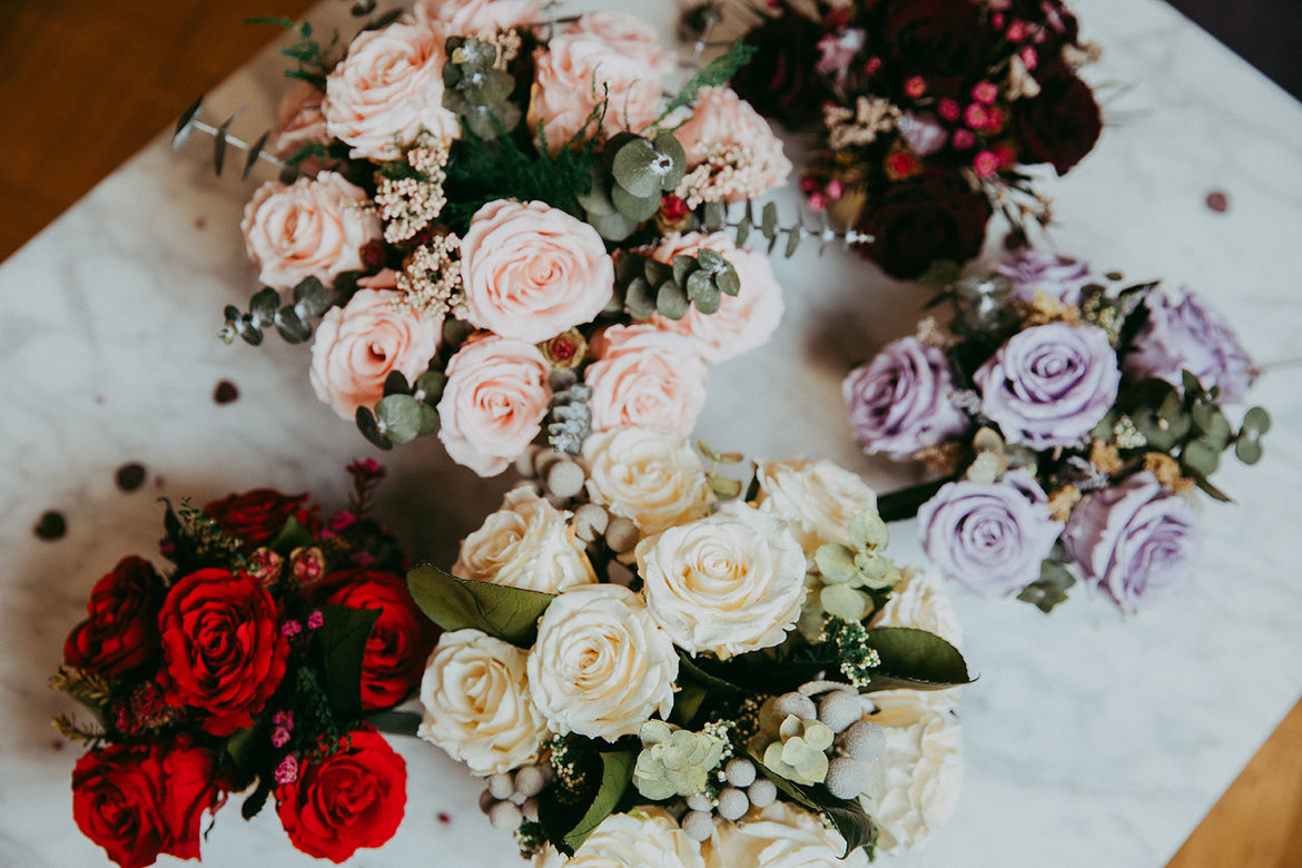Five bouquets of roses in red, pink, white, and lavender on a marble surface.