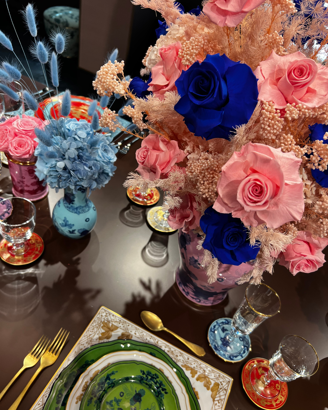 A floral table setting with pink and blue roses, gold cutlery, and green decorative plates.