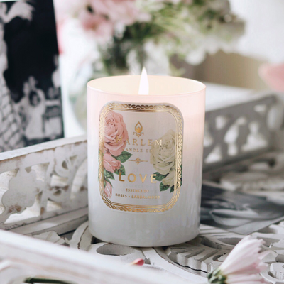 White candle labeled Love with roses, lit on a decorative white tray with flowers nearby.