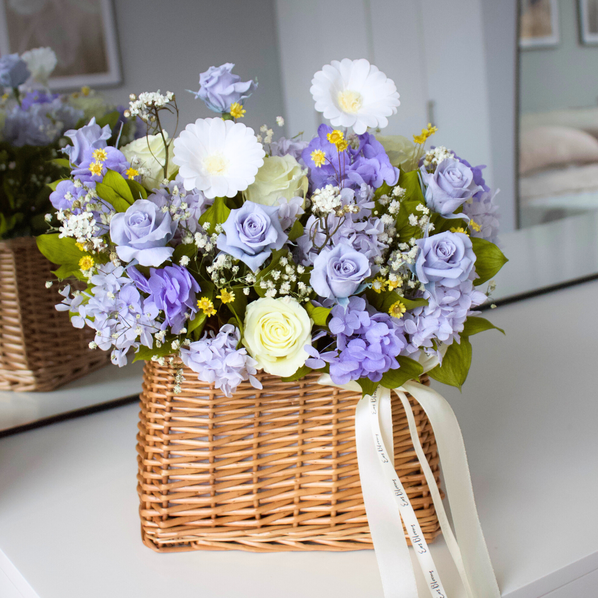 The Revival | Spring Basket by Eos Blooms: preserved purple, white & yellow flowers on a table.