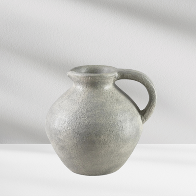The Eos Blooms Athens Vase, textured gray with a handle, sits on a white surface.