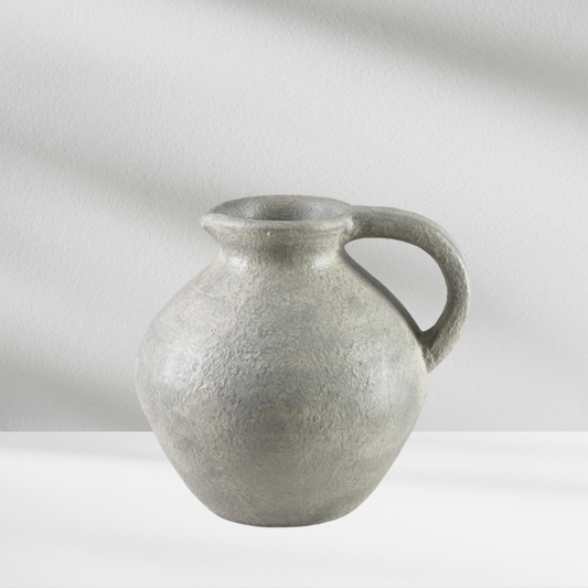 The Eos Blooms Athens Vase, textured gray with a handle, sits on a white surface.