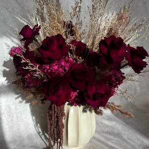 Bouquet of red flowers and dried grasses in a white vase on a light background