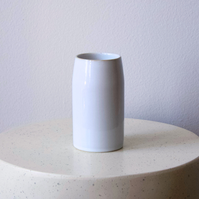 A white mug next to the Chelsea Vase by Eos Blooms sits on a round, pale table and backdrop.