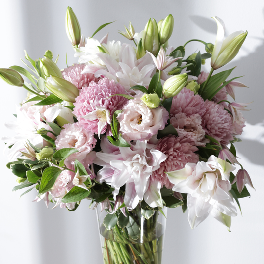 A bouquet of pink and white flowers in a glass vase against a light background.