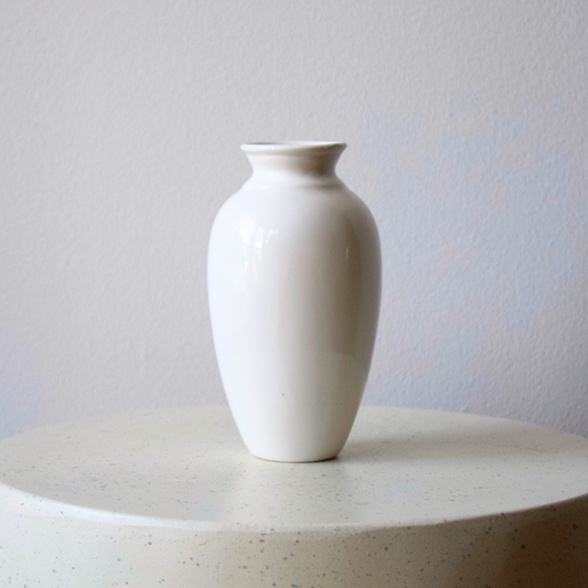 The Ginger Vase by Eos Blooms rests on speckled stone, its white ceramic minimalist and chic.