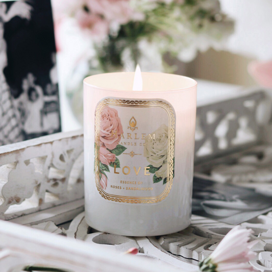 White candle labeled Love with roses, lit on a decorative white tray with flowers nearby.