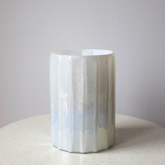 Iridescent Vase by Eos Blooms with fluted design on a speckled surface against plain wall.