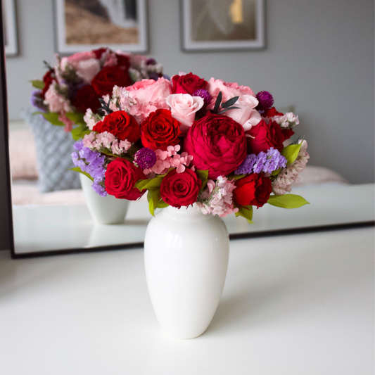 Eos Blooms' Ma Chérie (Petite), a white vase of red, pink, and purple flowers, sits on a table.