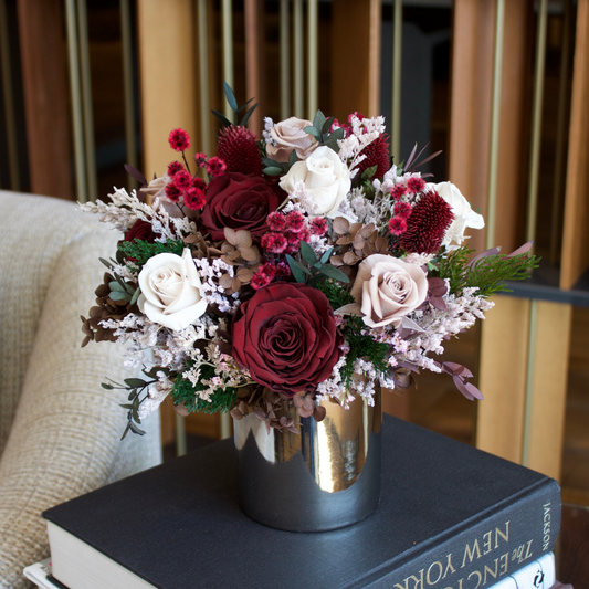 Eos Blooms’ Midnight Forest (Petite): winter red & white bouquet in a metallic vase on books.