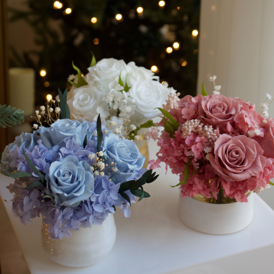 Three Mini vases by Eos Blooms with lasting blue, pink & white blooms on a white table.