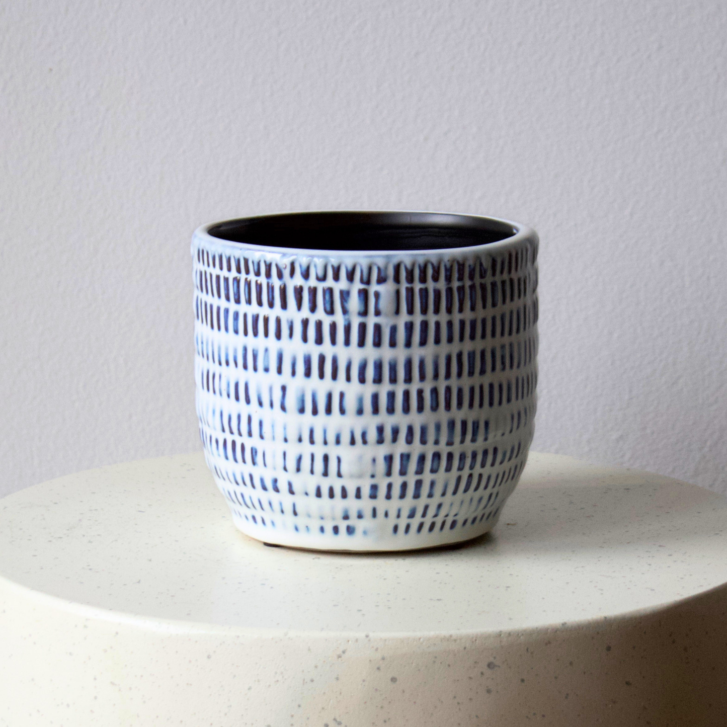 Blue and white Positano Vase by Eos Blooms on a round light surface against a plain wall.