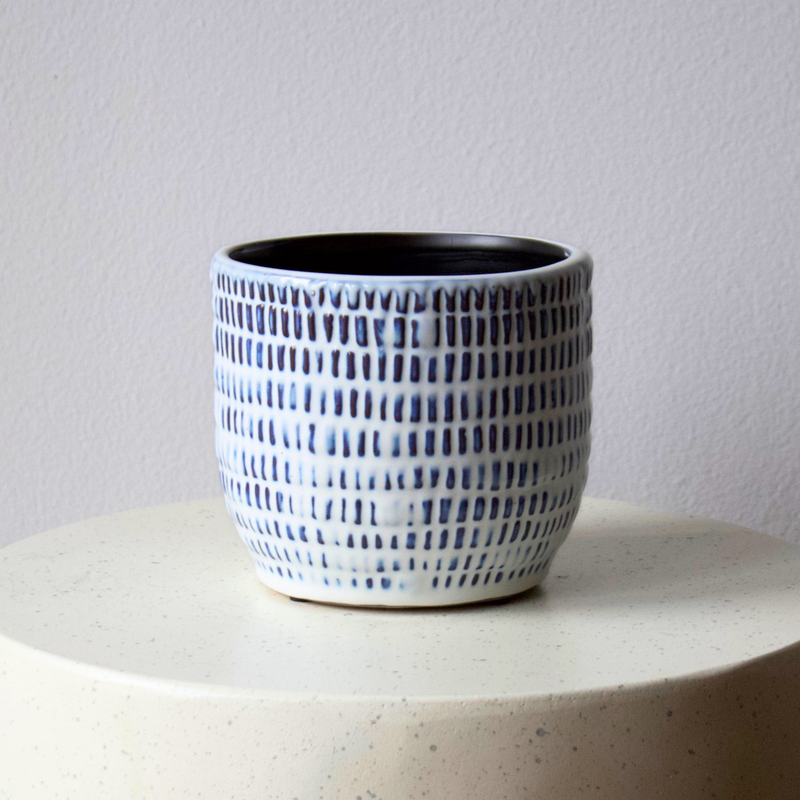 Blue and white Positano Vase by Eos Blooms on a round light surface against a plain wall.
