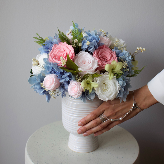 A hand touches an Eos Blooms Preserved Flower Subscription on a round white table.