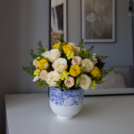 Bouquet of yellow and white roses in a blue and white vase on a white table.