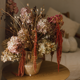 Eos Blooms Preserved Hydrangeas in a vase on a wooden table beside a beige sofa.