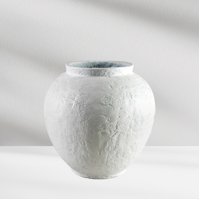 The Santorini Vase by Eos Blooms is a round, textured white ceramic piece on a white surface.