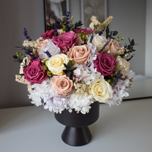 A bouquet of pink, white, and purple roses in a black vase on a white table.