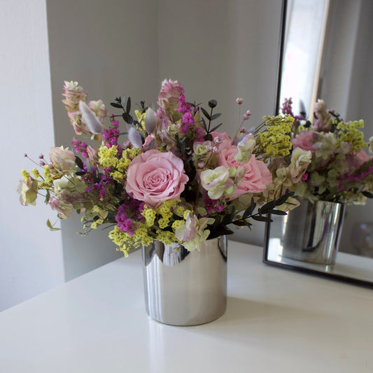 The Avonlea (Petite) by Eos Blooms, a silver vase with preserved roses, sits near a mirror.