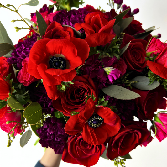 The Bisous by Eos Blooms: romantic red roses, anemones & purple blooms with green leaves.