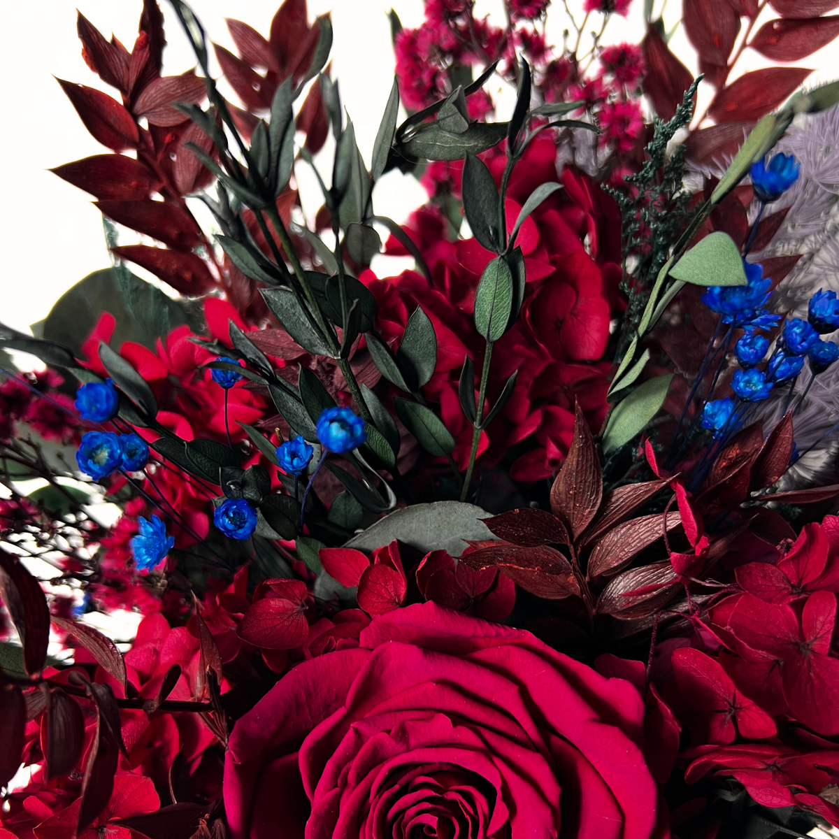 The Cerise (Petite) by Eos Blooms: red and blue preserved flowers with green burgundy leaves.