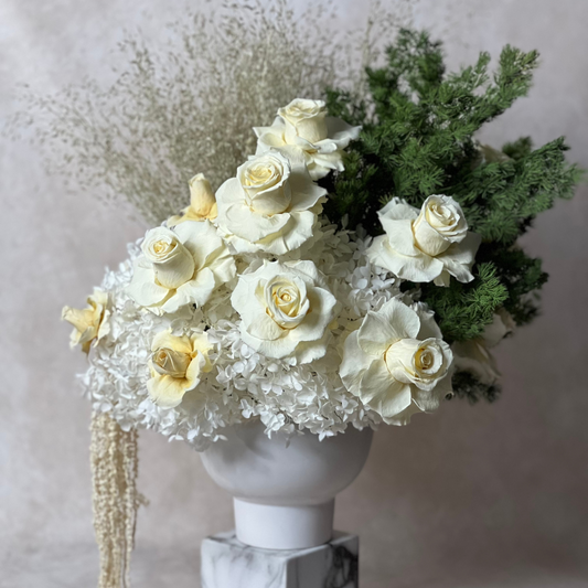 The Charlotte by Eos Blooms: white preserved roses and greenery in a white vase on marble.
