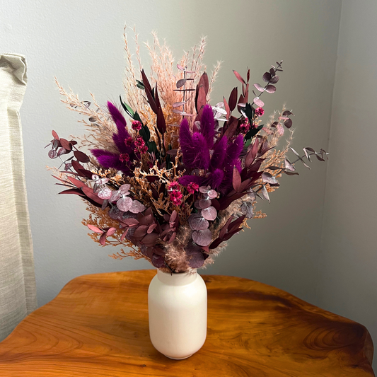 The Evelyn by Eos Blooms: dried purple, pink & beige flowers in a white vase on wood table.