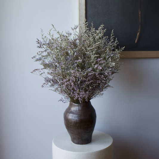 The Haven | Preserved Limonium by Eos Blooms in a dark ceramic vase on a white table.