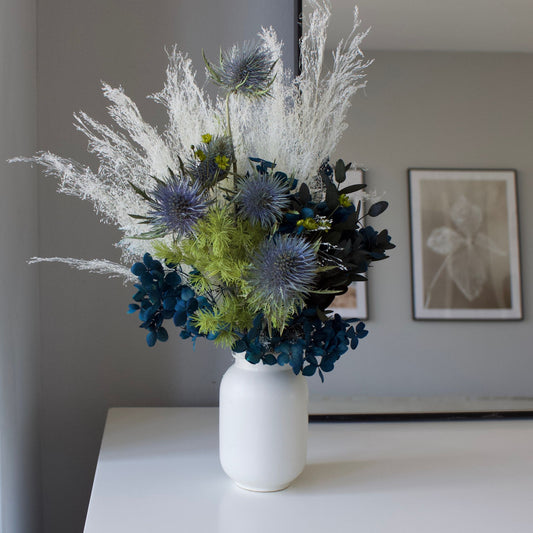 The Highlands by Eos Blooms: a white vase with preserved flowers on a white table and gray wall.