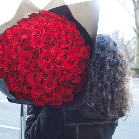 Person with curly hair holds Eos Blooms' The Hundred red rose bouquet, outdoors, from behind.