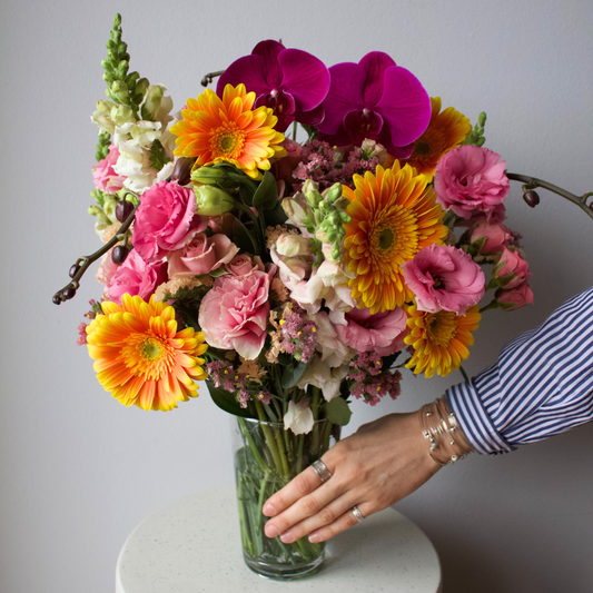 A hand arranges The Kindred by Eos Blooms, a pet-friendly bouquet, in a glass vase.