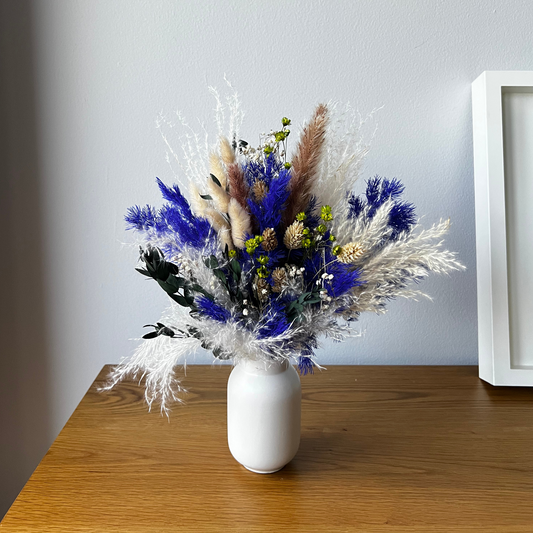 The Lazuli by Eos Blooms features royal blue preserved flowers in a white vase on a wood table.