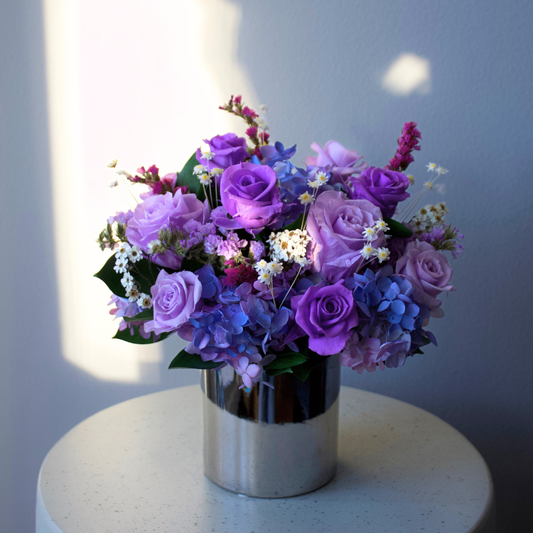 The Liminal (Petite) by Eos Blooms: a silver vase with blue blooms on a white table.