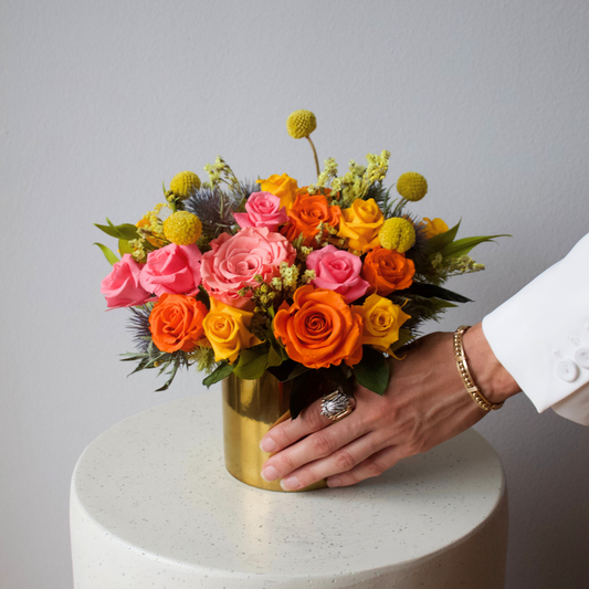 A hand with rings and a bracelet reaches for The Remi (Petite) by Eos Blooms.