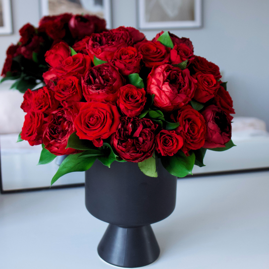 The Sybarite by Eos Blooms: a black vase with vibrant preserved roses and green leaves.
