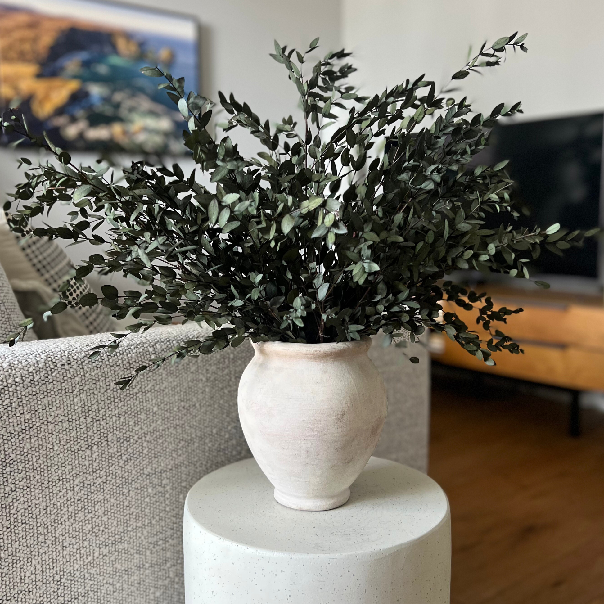 The Woodlands Preserved Parvifolia Eucalyptus by Eos Blooms in a white vase on a round table.