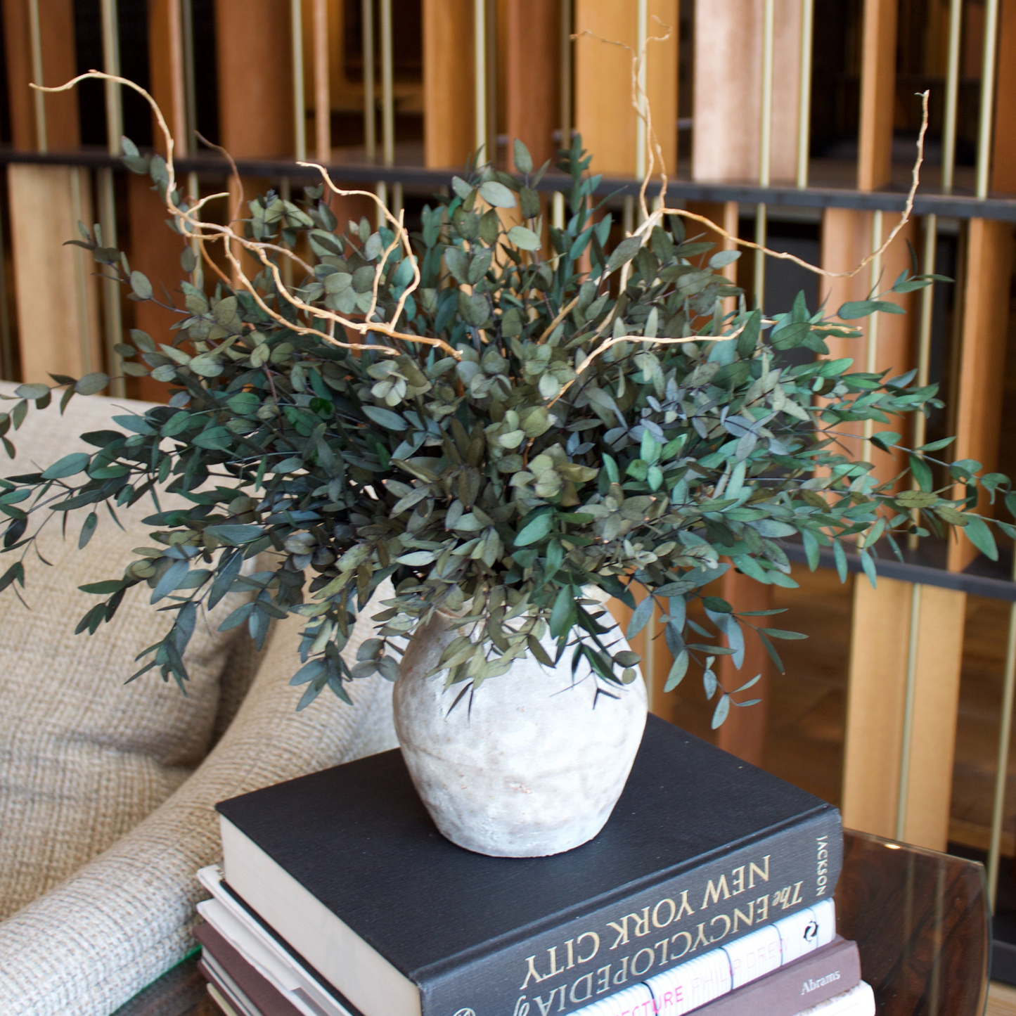 The Woodlands preserved Parvifolia Eucalyptus by Eos Blooms on books beside a modern couch.