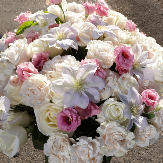 Bouquet of white, blush, and pink flowers arranged closely together on a sunlit surface.