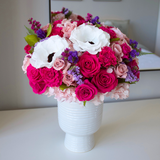 The Zenith is a white ceramic vase arranged with preserved Forever Roses, white anemones, purple blooms, and greenery—a long-lasting floral display perfect for any space.